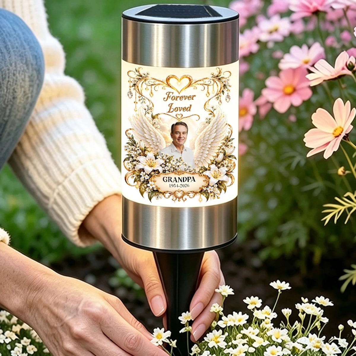 Hand placing a memorial solar garden light with grandpa photo among flowers