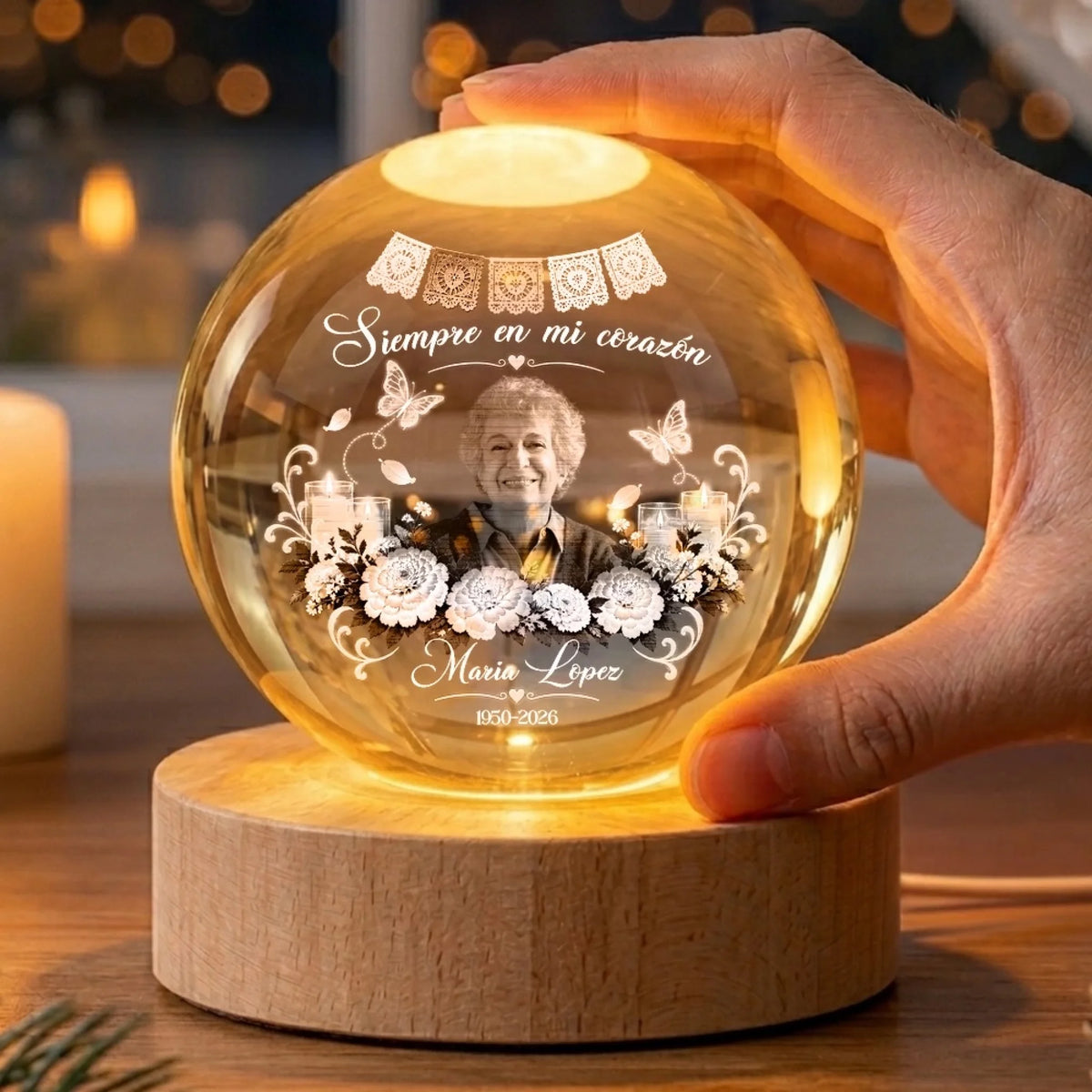 Hand resting on glowing memorial globe lamp engraved with Siempre en mi corazón