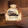 Glowing engagement night light on a bedside table beside a hand with ring