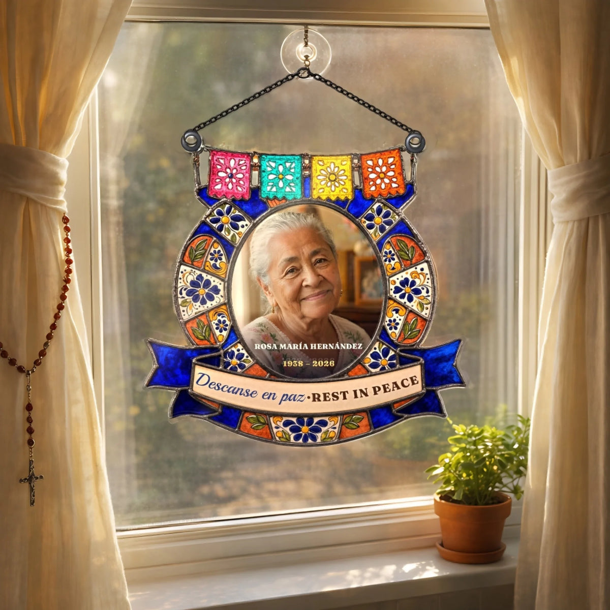 Talavera memorial suncatcher hanging in a window beside a rosary