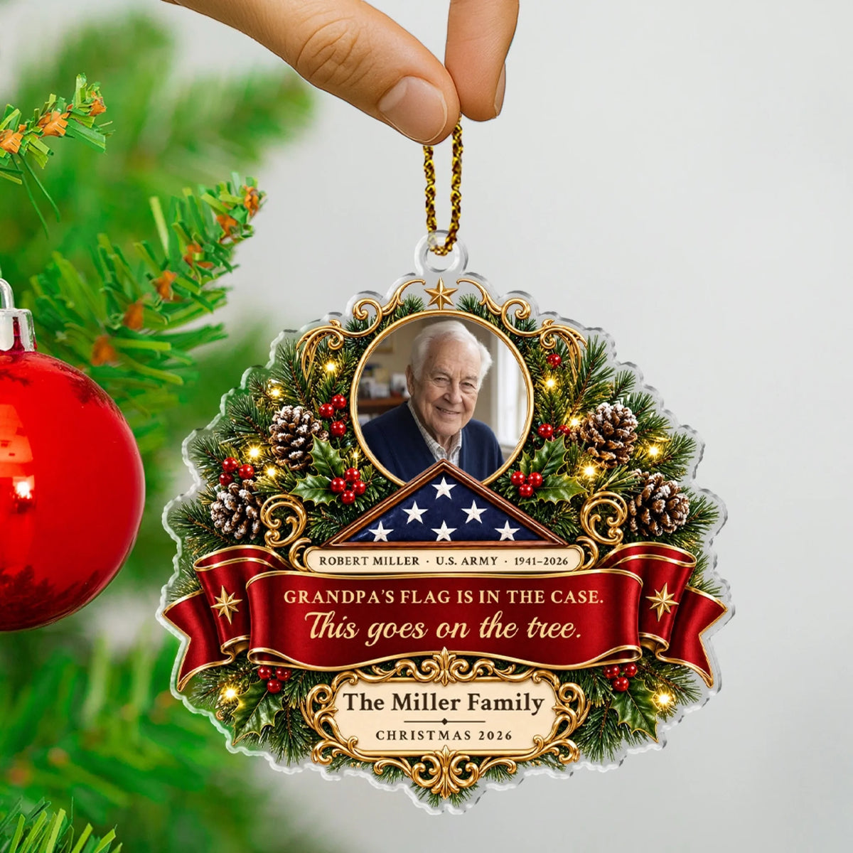 Fingers hanging the personalized veteran ornament by its rope beside a red Christmas bauble