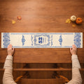 Hands smoothing the blue and white memorial table runner across a wooden table with small pumpkins