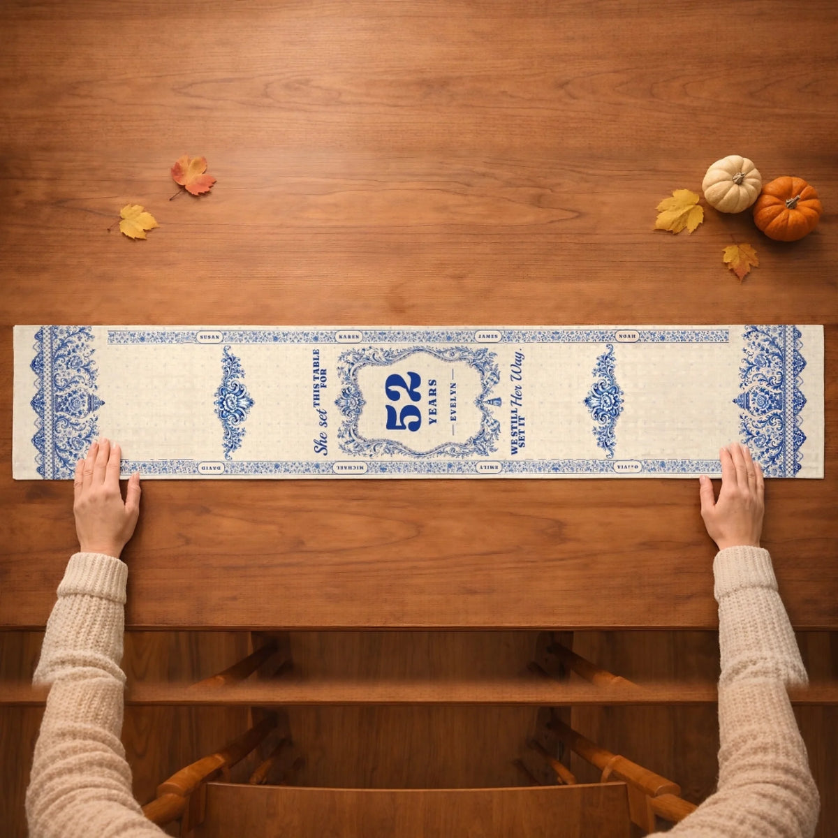 Hands smoothing the blue and white memorial table runner across a wooden table with small pumpkins