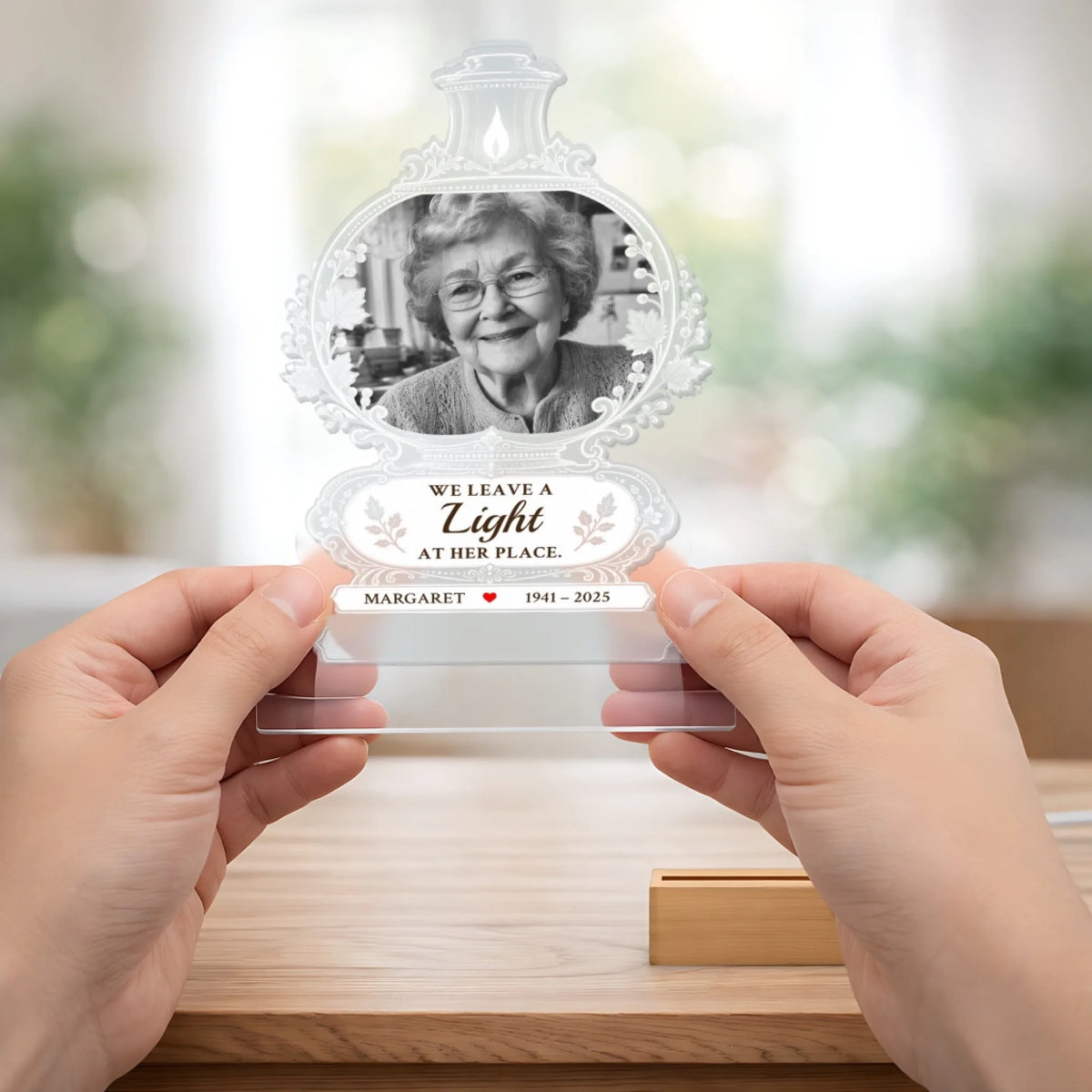 Hands holding the lamp-shaped memorial acrylic panel with photo, quote and name above its wooden base