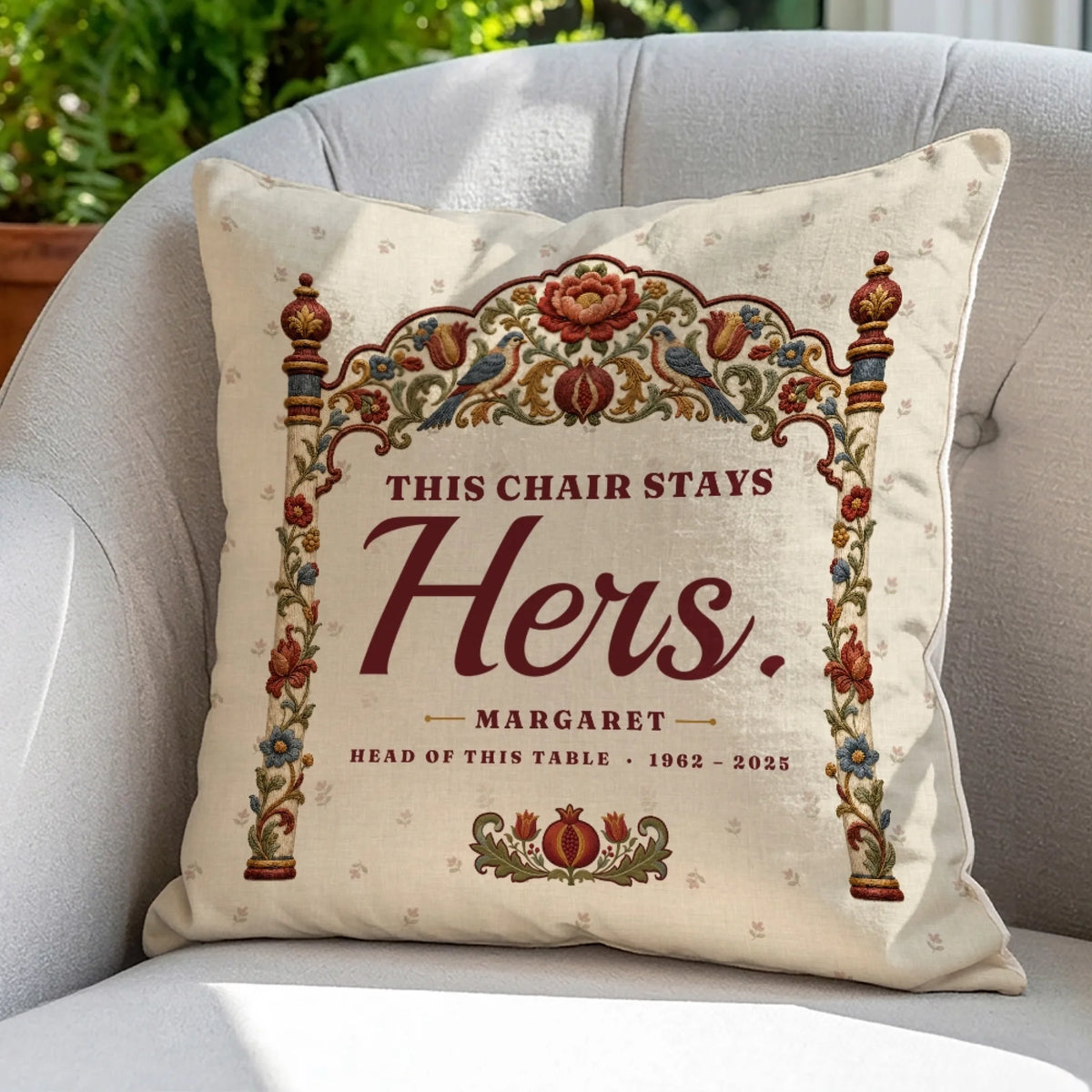 Folk embroidery memorial pillow with name and years on a gray armchair