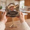 Hands holding cowboy hat memorial plaque above its wooden stand