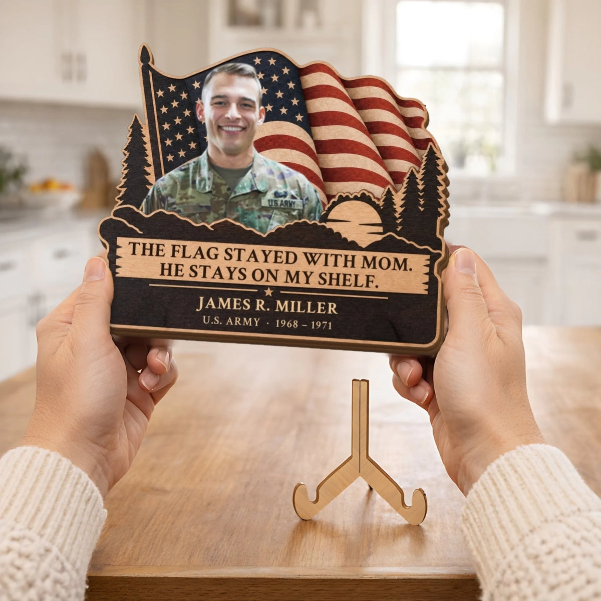 Hands holding veteran memorial plaque above its wooden stand in a kitchen