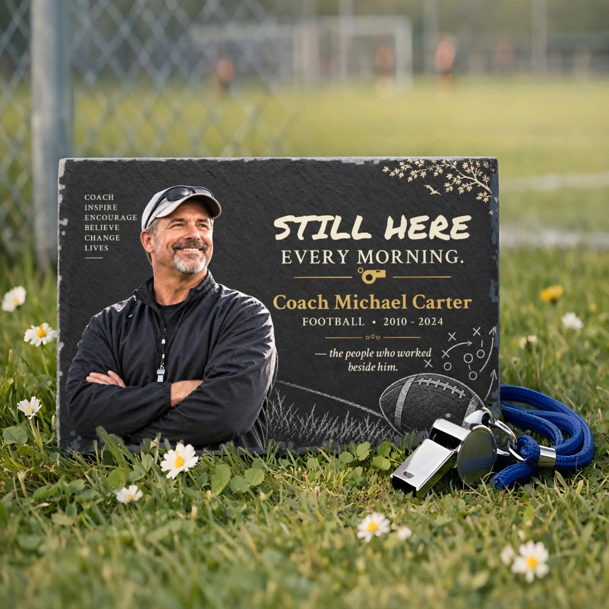 Personalized coach memorial stone on grass beside a whistle near a sports field